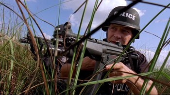 Movie still from “2 Fast 2 Furious” (2003), directed by John Singleton – A police officer is holding a rifle in the grass; Close Up shot, Low angle