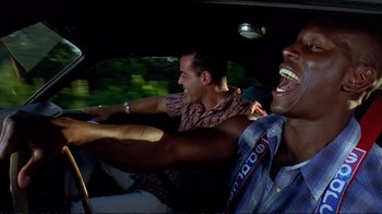 Movie still from “2 Fast 2 Furious” (2003), directed by John Singleton – Two men are driving in a car and one is laughing; Medium shot, Low angle