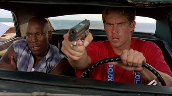 Movie still from “2 Fast 2 Furious” (2003), directed by John Singleton – A man holding a gun while sitting in the driver's seat of a car; Close Up shot, Over the shoulder angle