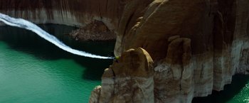 Movie still from “6 Underground” (2019), directed by Michael Bay – A person in the air with a surfboard in front of a body of water; Extreme Wide shot, High angle