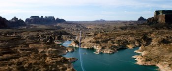 Movie still from “6 Underground” (2019), directed by Michael Bay – A jet plane flying over a body of water near mountains; Extreme Wide shot, High angle