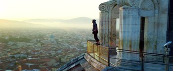 Movie still from “6 Underground” (2019), directed by Michael Bay – A man standing on top of a pillar on top of a building; Wide shot, Low angle