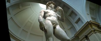 Movie still from “6 Underground” (2019), directed by Michael Bay – A statue of a naked man in a room with white walls; Wide shot, Low angle