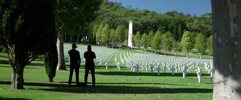 Movie still from “6 Underground” (2019), directed by Michael Bay – Two men standing in front of a field of white graves; Extreme Wide shot, High angle