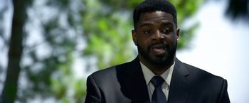 Movie still from “6 Underground” (2019), directed by Michael Bay – A man wearing a suit and tie with trees in the background; Close Up shot, Over the shoulder angle