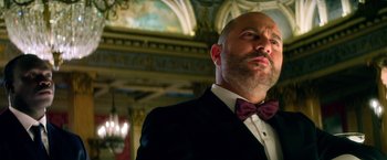 Movie still from “6 Underground” (2019), directed by Michael Bay – A man in a suit and bow tie looking up; Close Up shot, Low angle