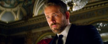 Movie still from “6 Underground” (2019), directed by Michael Bay – A person wearing a suit and tie; Close Up shot, Low angle