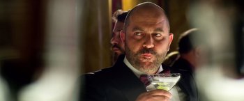 Movie still from “6 Underground” (2019), directed by Michael Bay – A man in a black suit holding a glass of wine; Close Up shot, Low angle