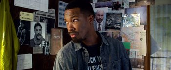 Movie still from “6 Underground” (2019), directed by Michael Bay – A man with a beard is standing in front of a wall with pictures; Close Up shot, Over the shoulder angle