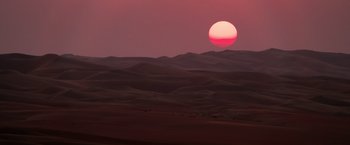 Movie still from “6 Underground” (2019), directed by Michael Bay – The sun is setting in the desert with a pink sky; Extreme Wide shot, High angle