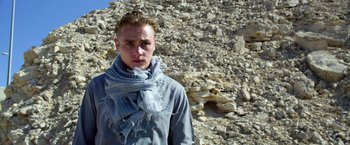 Movie still from “6 Underground” (2019), directed by Michael Bay – A man wearing a scarf standing in front of a pile of rocks; Close Up shot, Low angle