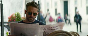 Movie still from “6 Underground” (2019), directed by Michael Bay – A man reading a newspaper while wearing sunglasses; Close Up shot, Over the shoulder angle