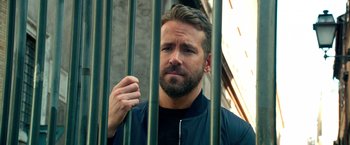 Movie still from “6 Underground” (2019), directed by Michael Bay – A person behind a metal fence; Close Up shot, Over the shoulder angle