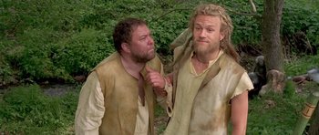 Movie still from “A Knight's Tale” (2001), directed by Brian Helgeland – Two men in medieval garb standing next to each other in a forest; Medium shot, Low angle