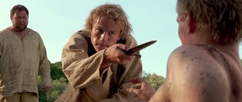 Movie still from “A Knight's Tale” (2001), directed by Brian Helgeland – A man holding a pair of scissors in one hand and a knife in the other; Close Up shot, Over the shoulder angle