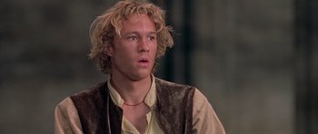 Movie still from “A Knight's Tale” (2001), directed by Brian Helgeland – A man with long blonde hair wearing a brown vest; Close Up shot, Low angle