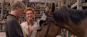 Movie still from “A Knight's Tale” (2001), directed by Brian Helgeland – A red headed man standing next to a brown horse; Medium shot, Low angle