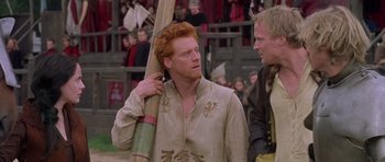 Movie still from “A Knight's Tale” (2001), directed by Brian Helgeland – A man with a red beard holding a wooden stick; Medium shot, Over the shoulder angle