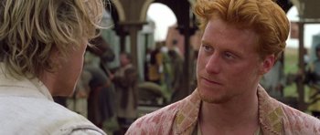 Movie still from “A Knight's Tale” (2001), directed by Brian Helgeland – A person wearing a suit and tie; Close Up shot, Over the shoulder angle