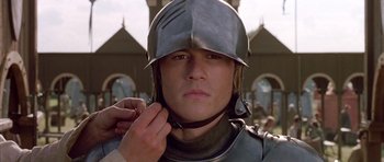 Movie still from “A Knight's Tale” (2001), directed by Brian Helgeland – A man wearing a helmet while putting on a chain; Close Up shot, Low angle