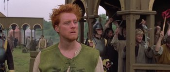 Movie still from “A Knight's Tale” (2001), directed by Brian Helgeland – A red headed man in a green vest and a crowd of people; Medium shot, Low angle
