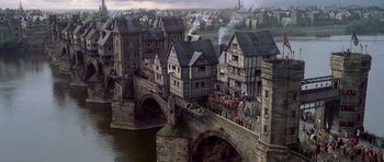 Movie still from “A Knight's Tale” (2001), directed by Brian Helgeland – An illustration of a medieval town with a bridge crossing the river; Extreme Wide shot, High angle