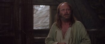 Movie still from “A Knight's Tale” (2001), directed by Brian Helgeland – A man with long hair and a beard is standing in front of a window; Close Up shot, Over the shoulder angle