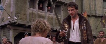 Movie still from “A Knight's Tale” (2001), directed by Brian Helgeland – A man holding a sword in front of a crowd; Medium shot, Over the shoulder angle