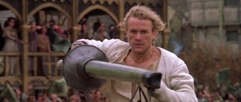 Movie still from “A Knight's Tale” (2001), directed by Brian Helgeland – A man in a white shirt is holding a metal object; Medium shot, Low angle