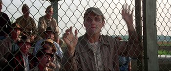 Movie still from “A League of Their Own” (1992), directed by Penny Marshall – A man is standing behind a chain link fence; Medium shot, Over the shoulder angle