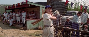 Movie still from “A League of Their Own” (1992), directed by Penny Marshall – A woman holding a baseball bat while standing next to a fence; Medium shot, Over the shoulder angle