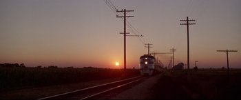 Movie still from “A League of Their Own” (1992), directed by Penny Marshall – A train traveling down train tracks next to power lines at sunset; Extreme Wide shot, Low angle