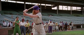 Movie still from “A League of Their Own” (1992), directed by Penny Marshall – A woman in a baseball uniform is holding a baseball bat in front of a group of people; Wide shot, Low angle