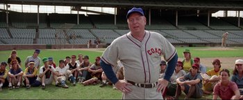 Movie still from “A League of Their Own” (1992), directed by Penny Marshall – An older baseball player standing in front of a group of people; Medium shot, Over the shoulder angle