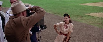 Movie still from “A League of Their Own” (1992), directed by Penny Marshall – A girl in a baseball uniform is being filmed by a cameraman; Medium shot, Over the shoulder angle