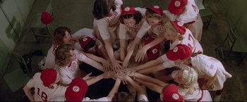 Movie still from “A League of Their Own” (1992), directed by Penny Marshall – A group of women in a circle with their hands in the center; Medium shot, Overhead angle
