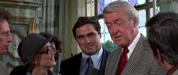 Movie still from “Airport '77” (1977), directed by Jerry Jameson – Two men and a woman are talking to each other in front of a stained glass window; Close Up shot, Over the shoulder angle
