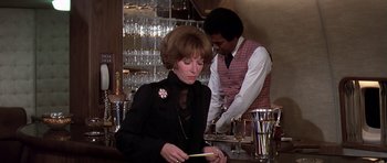 Movie still from “Airport '77” (1977), directed by Jerry Jameson – A woman in a black dress and a man in a red vest are at a bar; Medium shot, Over the shoulder angle