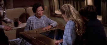 Movie still from “Airport '77” (1977), directed by Jerry Jameson – A woman sitting at a table talking to another woman; Medium shot, Over the shoulder angle