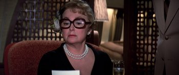 Movie still from “Airport '77” (1977), directed by Jerry Jameson – An older woman wearing glasses and a pearl necklace sitting at a table; Close Up shot, Over the shoulder angle