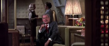 Movie still from “Airport '77” (1977), directed by Jerry Jameson – An older man sitting on a chair in a room; Medium shot, Over the shoulder angle
