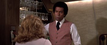 Movie still from “Airport '77” (1977), directed by Jerry Jameson – A man in a vest and tie talking to a woman in front of a bar; Close Up shot, Over the shoulder angle