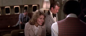 Movie still from “Airport '77” (1977), directed by Jerry Jameson – A woman sitting next to a man wearing a suit; Medium shot, Over the shoulder angle