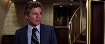 Movie still from “Airport '77” (1977), directed by Jerry Jameson – A man in a suit and tie standing in front of a painting; Close Up shot, Over the shoulder angle