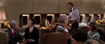 Movie still from “Airport '77” (1977), directed by Jerry Jameson – A group of people sitting around a table in a room; Wide shot, High angle