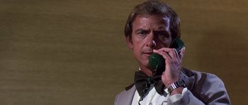 Movie still from “Airport '77” (1977), directed by Jerry Jameson – A man wearing a bow tie talking on a phone; Close Up shot, Low angle
