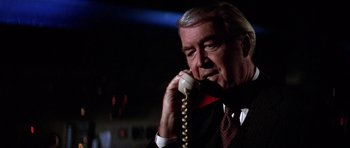 Movie still from “Airport '77” (1977), directed by Jerry Jameson – An older man talking on a phone while wearing a suit and tie; Close Up shot, Low angle