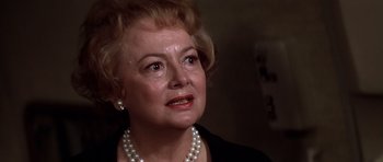 Movie still from “Airport '77” (1977), directed by Jerry Jameson – An older woman wearing a black jacket and a pearl necklace; Close Up shot, Over the shoulder angle