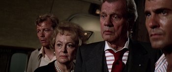 Movie still from “Airport '77” (1977), directed by Jerry Jameson – An older man and a younger woman standing next to each other; Close Up shot, Low angle