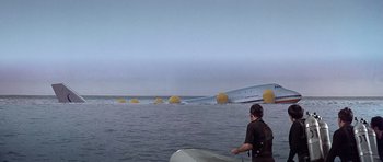Movie still from “Airport '77” (1977), directed by Jerry Jameson – A man standing on top of a surfboard in the water; Extreme Wide shot, Low angle